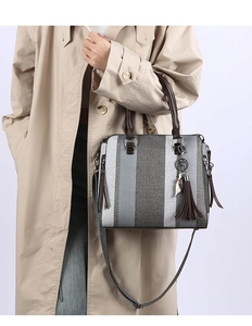Detailed view of gray striped tote bag with brown handles and feather tassel charm decoration