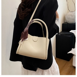 Dettaglio della borsa beige in pelle martellata con foulard decorativo in seta sul manico