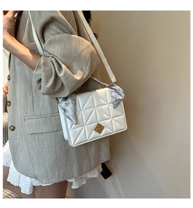Close-up of white quilted crossbody bag with gold lock and decorative paisley silk scarf