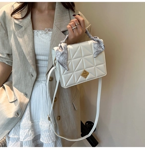 Detail of white quilted crossbody bag featuring gold clasp and silk scarf handle