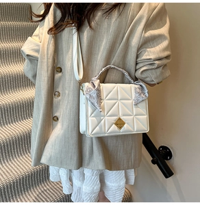 Detailed shot of white quilted shoulder bag with scarf-wrapped handle on a model