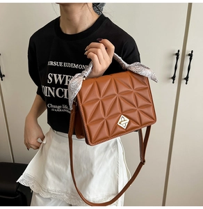 Detail of a brown quilted crossbody bag featuring a golden buckle and silk scarf handle