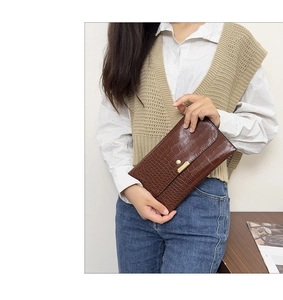 Detailed texture of dark brown faux crocodile leather clutch with gold metal buckle