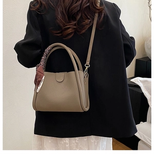 Dettaglio della borsa a secchiello in pelle taupe con trama a grana e foulard decorativo