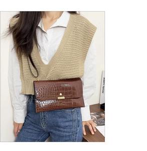 Detail of a dark brown crocodile texture envelope bag with a stylish gold buckle accent