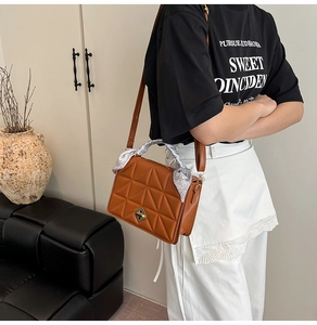 Detail of brown quilted shoulder bag with gold clasp and silk scarf handle accent