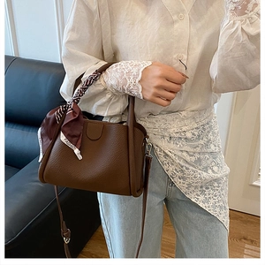 Dettaglio di una borsa a secchiello in pelle marrone con foulard stampato e tracolla lunga