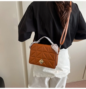 Detail of a brown quilted crossbody bag with gold lock and stylish scarf wrap handle