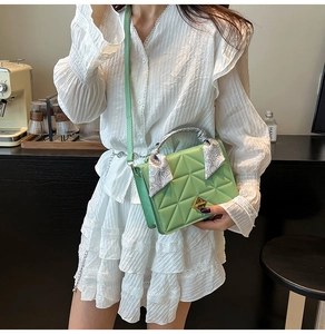 Close-up of light green quilted crossbody bag with golden clasp and silk scarf handle
