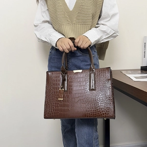 Detail of dark brown crocodile pattern tote bag with gold metal hardware and top handles