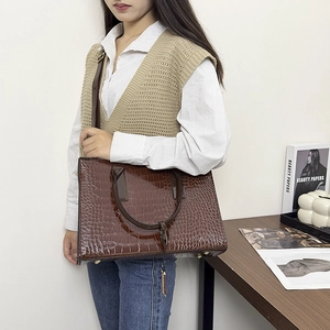 Detail of dark brown crocodile texture tote bag with golden feet and shoulder strap