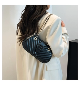 Detail of black quilted crossbody bag featuring V-shaped stitching and gold chain strap