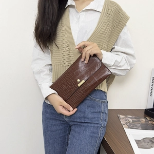 Detail of a brown crocodile pattern envelope clutch with a luxury gold metal buckle