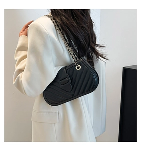 Shoulder view of a black quilted crossbody bag with chain strap on white blazer