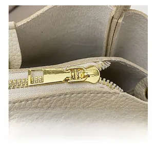Dettaglio ravvicinato della cerniera dorata su borsa a secchiello in pelle beige