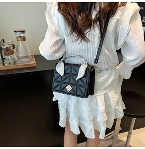 Detail of black quilted crossbody bag with silk ribbon handle and silver turn-lock