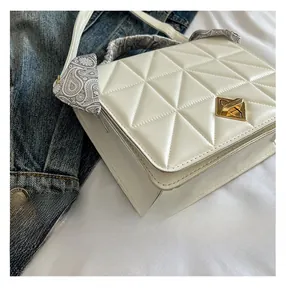 Detail of white quilted crossbody bag with golden twist lock and silk scarf handle wrap