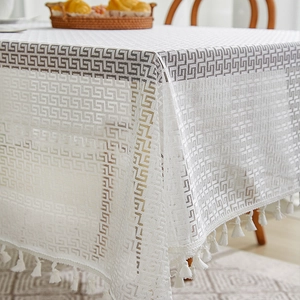 Close-up of white lace tablecloth with black Greek key patterns and fringe edges