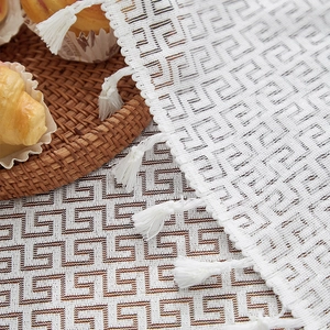 Detail of white cotton linen tablecloth with Greek key pattern and elegant fringe tassels