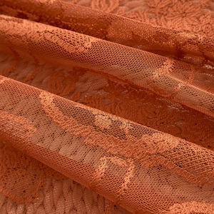 Detailed macro shot of burnt orange lace curtain fabric with floral embroidery