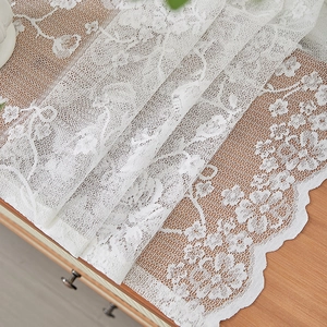 Detail of white French lace curtain featuring elegant floral patterns and wavy edges
