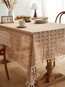 Detail of warm beige lace tablecloth with geometric hollow patterns and white cotton tassels