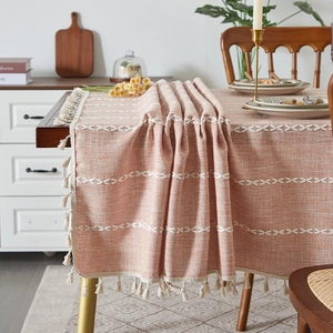 Close-up of bohemian linen tablecloth featuring white geometric embroidery and tassels