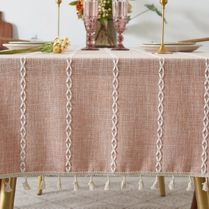 Detail of orange linen tablecloth with white embroidery stripes and elegant cream tassels