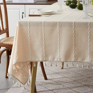 Close-up of beige linen tablecloth featuring woven stripes and elegant fringe trim details