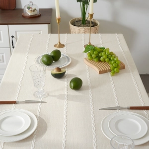 Detailed texture of beige linen tablecloth with white embroidered stripes and tassels