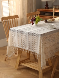 Detail of bohemian beige lace tablecloth with geometric hollow patterns and tassels