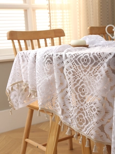 Detailed macro of white bohemian lace tablecloth featuring floral hollow patterns and tassels