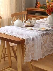 Close-up of white lace table runner with leaf pattern and elegant beige fringe trim