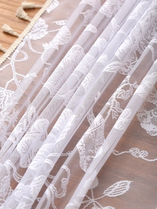 Detailed macro view of white bohemian lace tablecloth featuring floral embroidery and tassels