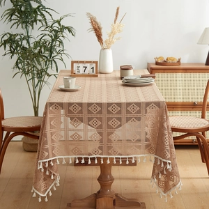 Boho style beige lace tablecloth with tassel edges on a warm rustic wooden dining table