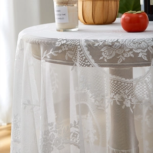 Close-up of white lace tablecloth with rose patterns and ruffle edges on a round table