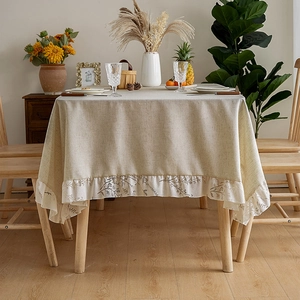 Detail of beige linen tablecloth with ruffled edges and brown floral embroidery motifs