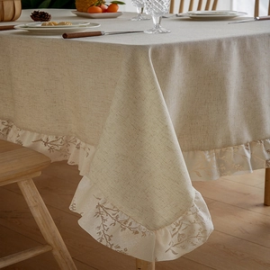 Close-up of khaki linen tablecloth with white lace floral embroidery and ruffled edges