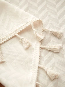 Close-up of cream rectangular tablecloth with decorative woven lace and tassels