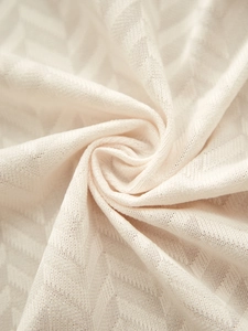Macro shot of cream-colored knitted tablecloth with herringbone texture and soft folds