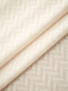 Close-up of beige herringbone textile fabric showing detailed weave and soft drape