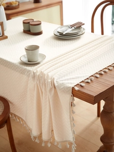 Detail of beige textured linen tablecloth with elegant tassels and herringbone weave