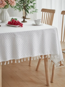 Detail shot of white jacquard tablecloth with elegant wave texture and tassel trim
