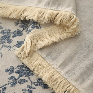 Detail of vintage linen tablecloth with blue floral print and decorative beige tassels