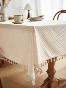 Detail of beige jacquard tablecloth with herringbone texture and elegant cream tassels