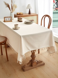 Detail of beige knit tablecloth featuring textured patterns and elegant woven fringe edges
