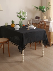 Close-up of black hollow lace tablecloth with delicate fringe trim on a white wood table