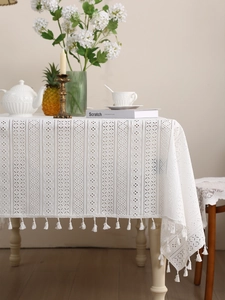 Detail of white hollow lace tablecloth with geometric patterns and fringe tassels