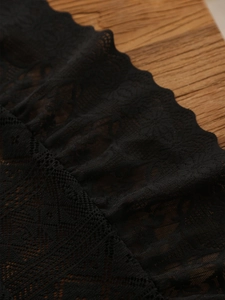 Detail of black floral lace with scalloped edges on a rustic wood background