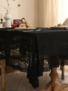 Detail of black lace tablecloth with geometric hollow patterns and ruffled edges on wood